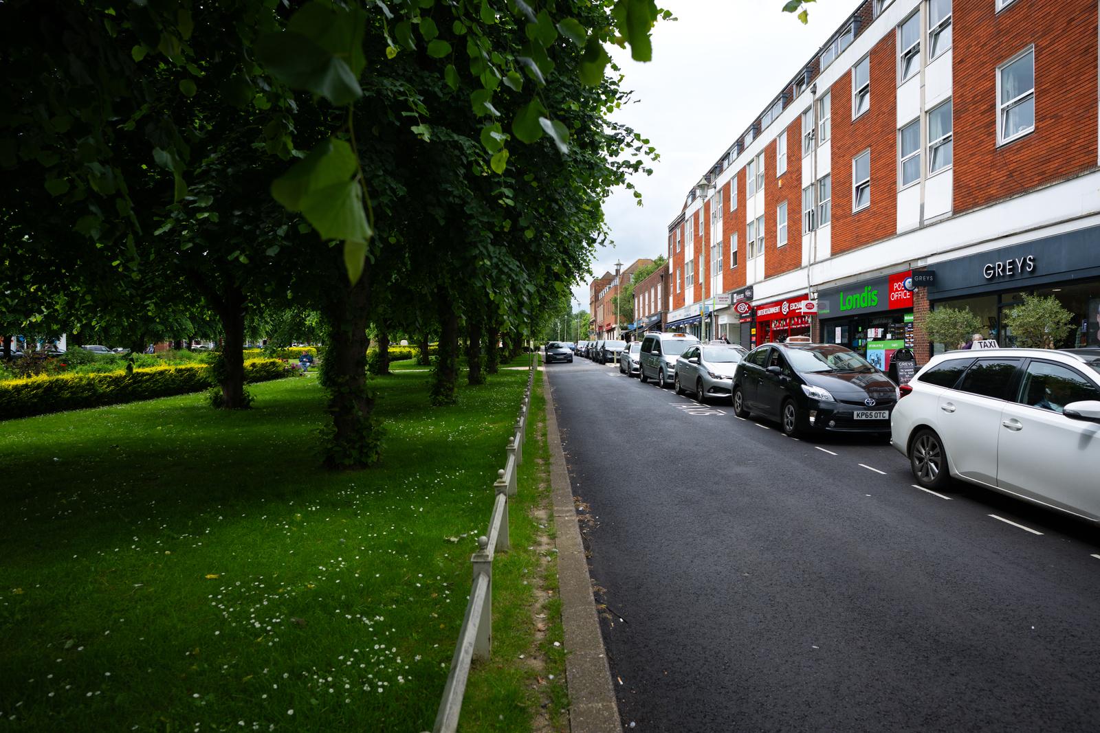Road in WGC with a field on the left and cars parked on the right side
